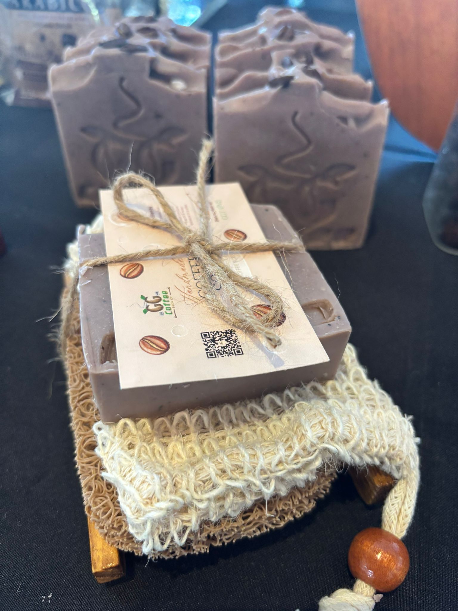 GG Coffee Soap Natural Exfoliant on a wooden base with soft sponge and woven pad, showcasing natural skincare.